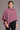 A model wearing a pink merino poncho with a diagonal detail and asymmetric neckline, giving luxurious warmth without weight from kiwi sheepskins