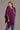 A person wearing a berry color possum merino split front wrap with a mulberry silk detail, paired with a grey sweater and blue jeans
