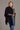 A model draping over a black Possum Merino Split Front Wrap from Kiwi Sheepskins Measuring approximately 80cm by 102cm, offering both style and comfort
