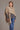 A person wearing a mocha possum merino split front wrap with a mulberry silk detail, paired with a grey sweater and blue jeans, delivering exceptional warmth while remaining lightweight