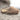 Pair of a brown Sheepskin Slippers with brand label and wooly interior made of sheepskin fur on a concrete surface #color_sand