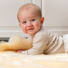 Baby lying on a soft sheepskin rug with a neutral background